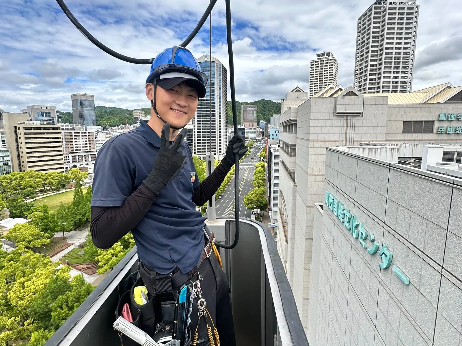 屋上の縁でロープを手にし、カメラに向かって笑う橙會の作業員
