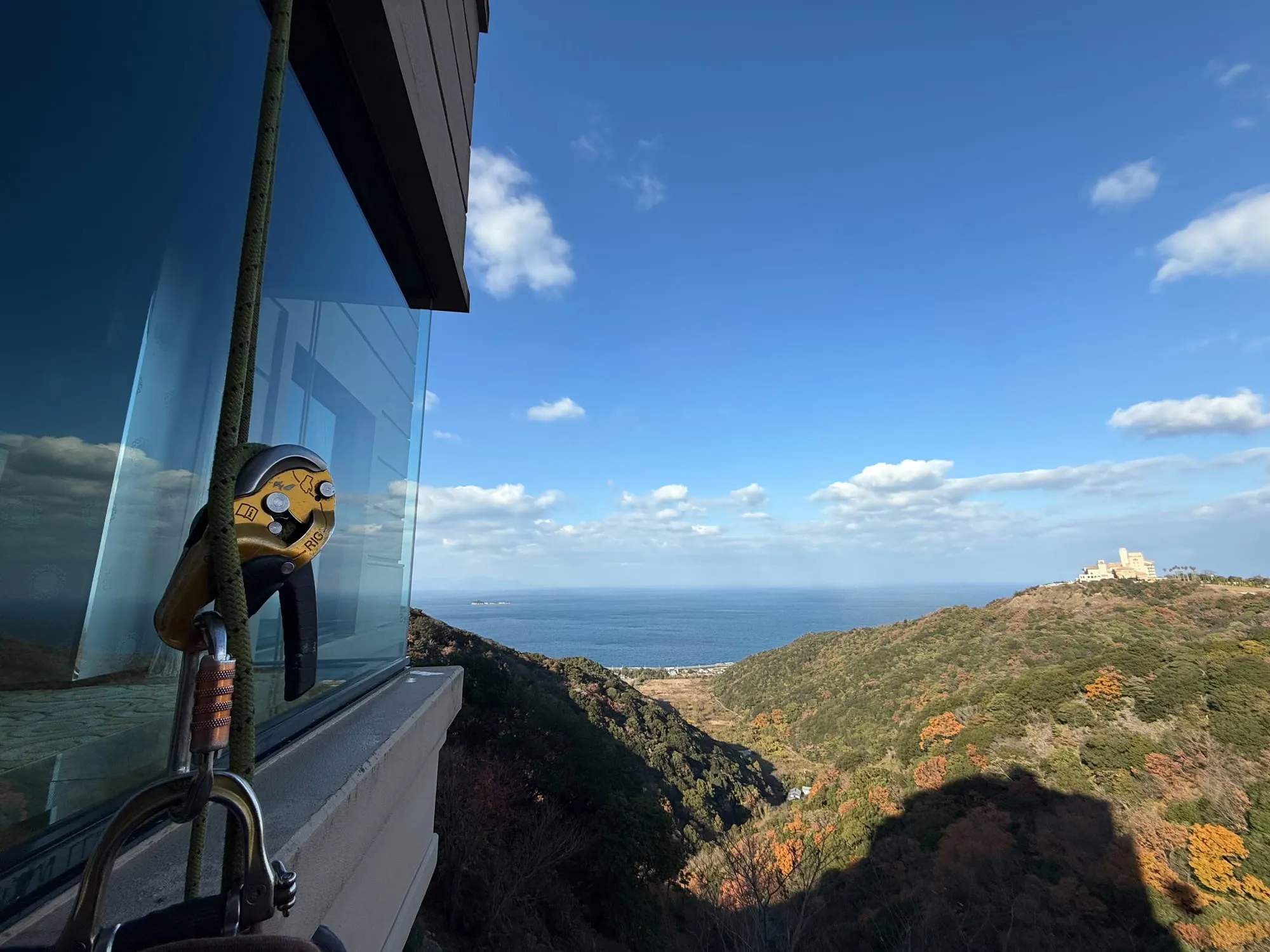 海と山が見える高所の窓際に掛けられた下降器とロープ