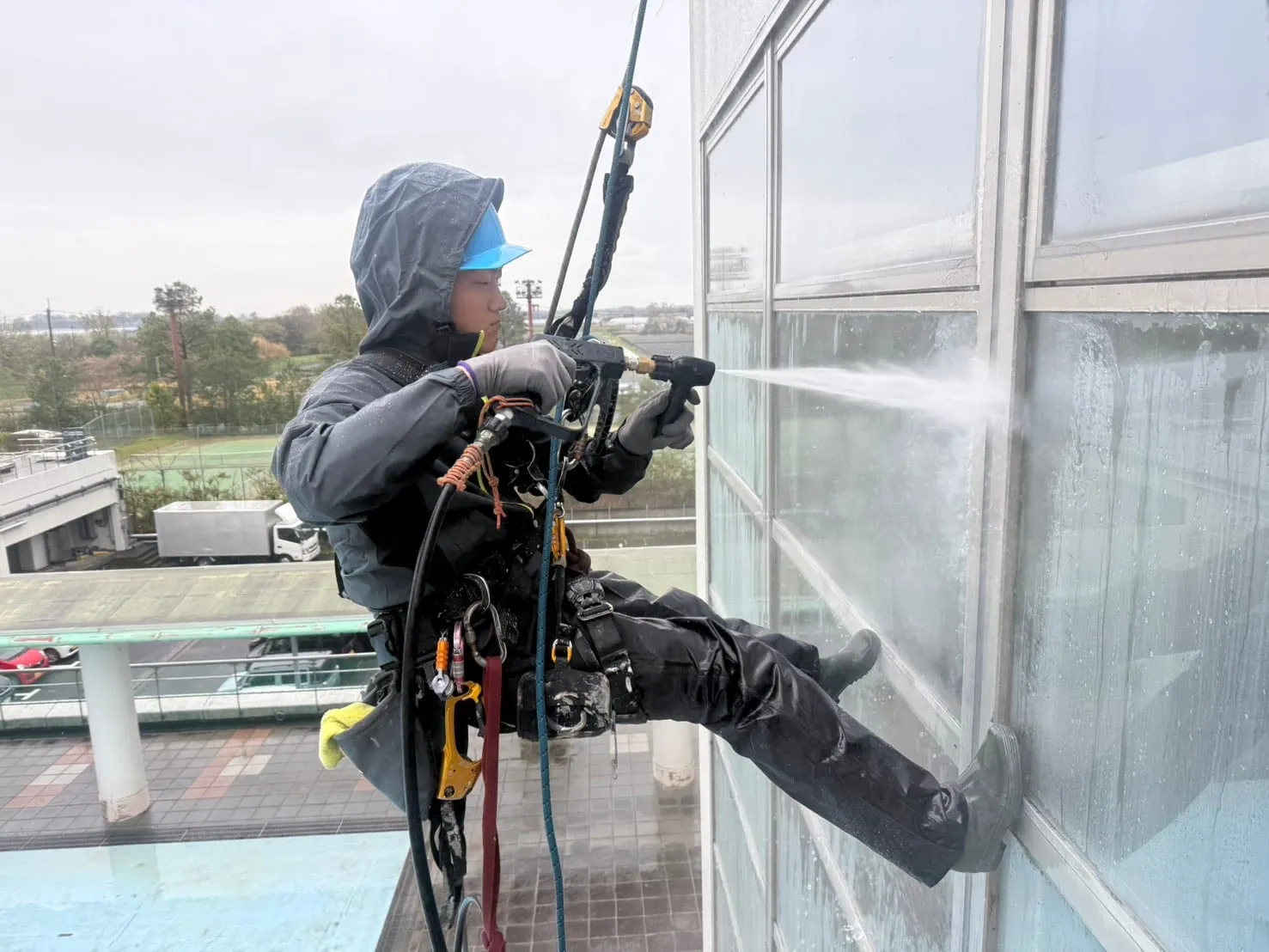 ロープで吊り下がりながら、高圧洗浄機で建物の壁面に水を吹き付ける作業員